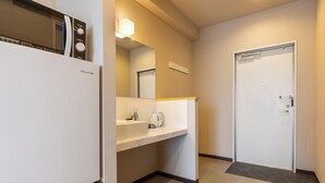 A modern hotel room with a white refrigerator, a sink with a kettle, and a door with a handle. - Mr.KINJO in GRAND BLUE CHATAN (Chatan)
