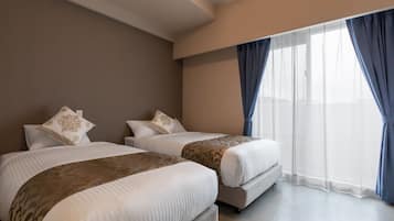 A hotel room with two beds, a large window with sheer curtains, and a neutral color scheme.