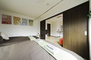 A modern hotel room with a large bed, a wooden door, and a view of the hallway.