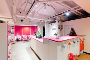 A modern interior with a reception desk, a pink sofa, and a decorative Christmas tree. - Nikko Inn Minamisenba 502 - Hostel (Osaka)