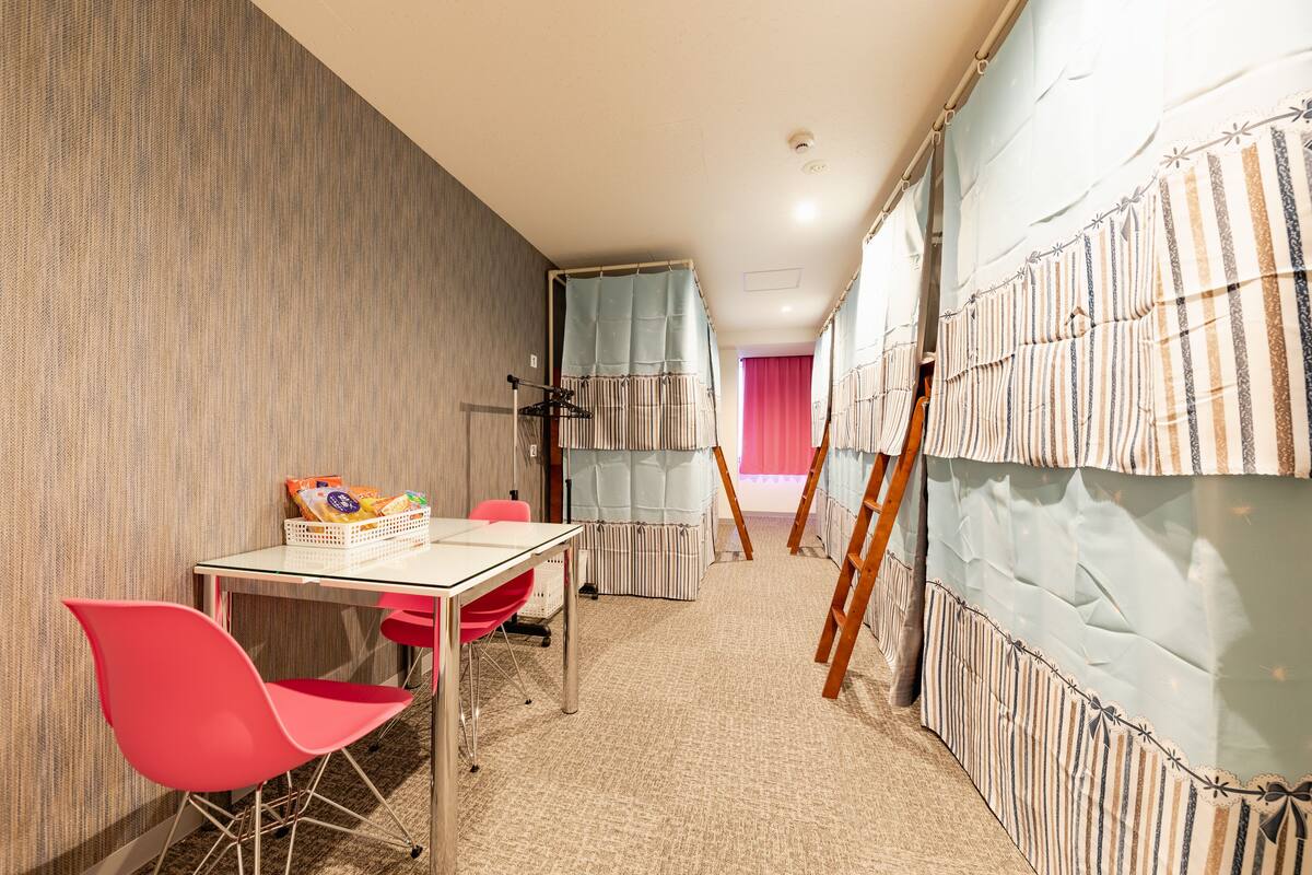 A room with a striped curtain, a table with a basket, a red chair, and a wooden ladder leaning against the wall.