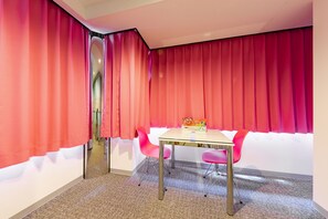 A room with a glass table, pink chairs, and red curtains. - Nikko Inn Minamisenba 503 - Hostel (Osaka)
