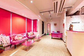A brightly lit reception area with a pink sofa, a glass coffee table, and a reception desk. - Nikko Inn Minamisenba 503 - Hostel (Osaka)