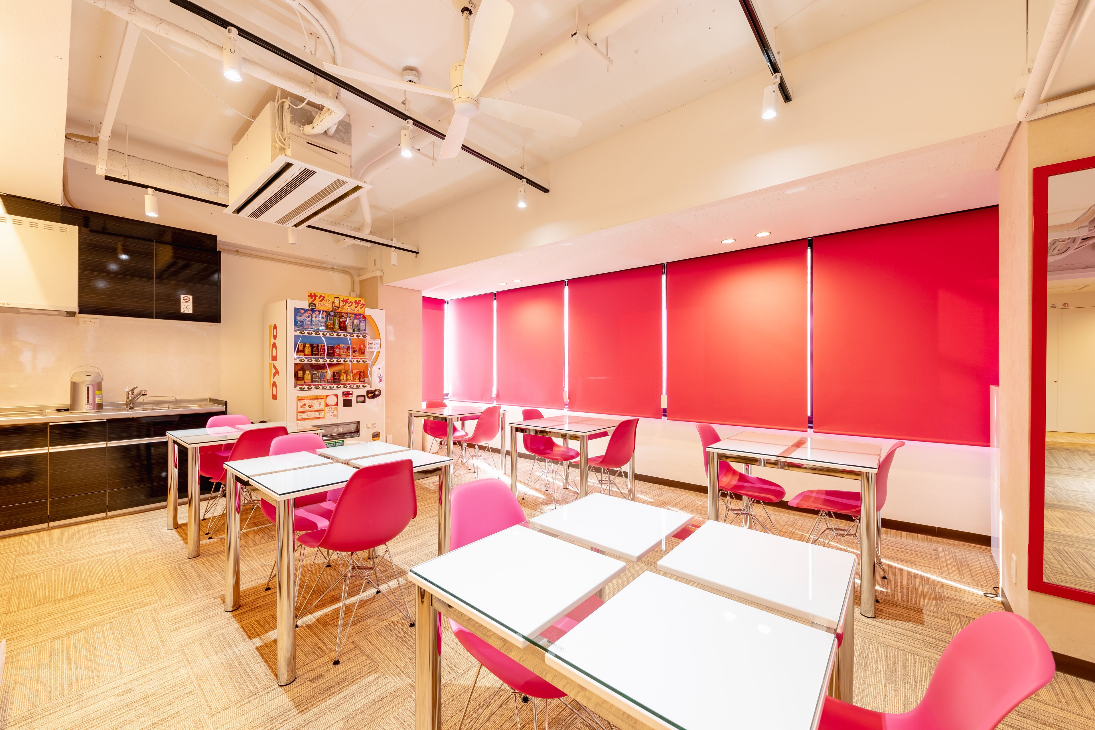 A modern dining area with red chairs and white tables, equipped with ceiling fans and recessed lighting.