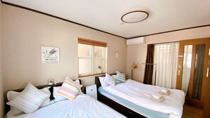 A hotel room with two beds, a window, an air conditioning unit, and a door with curtains. - Nestle Suite Tokyo Shinokubo (Tokyo)