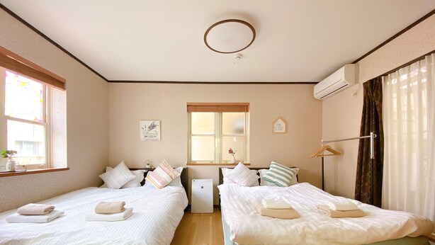 A hotel room with two beds, a window, an air conditioning unit, and a bedside table. - Nestle Suite Tokyo Shinokubo (Tokyo)