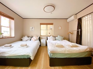 A hotel room with two beds, a window, an air conditioning unit, and a bedside table.