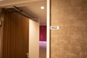 A hotel room with a wooden panel wall, a ceiling-mounted light fixture, and a wall-mounted number sign indicating room 602. - Nikko Inn Minamisenba 602 - Hostel, Caters to Women (Osaka)