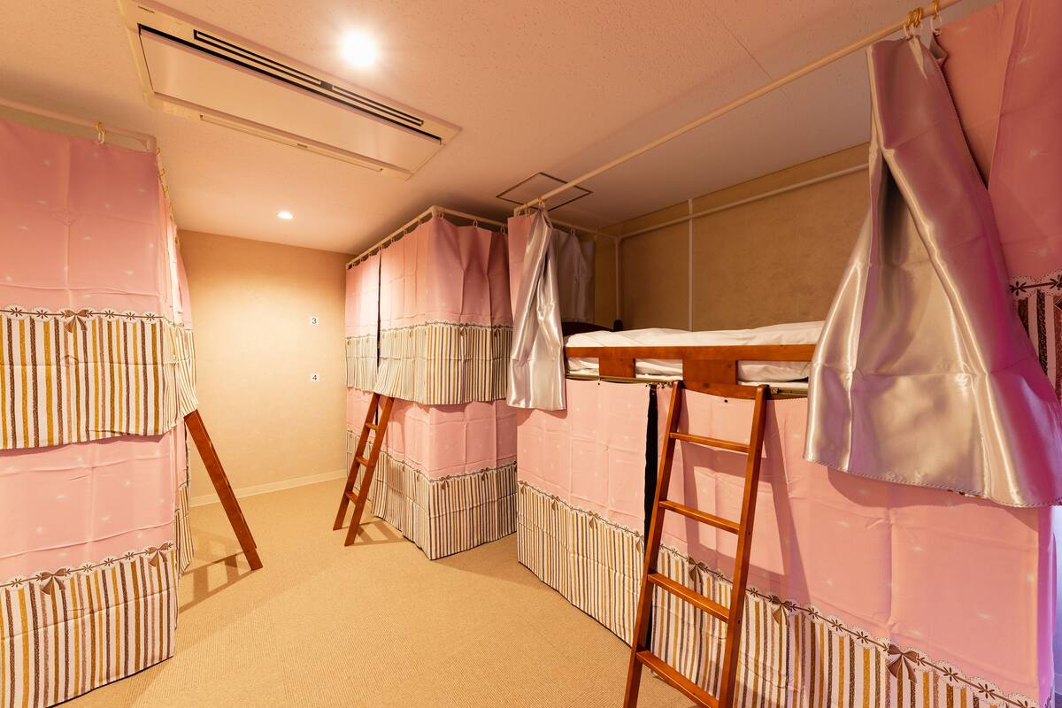 A room with bunk beds, a ladder, and pink curtains.