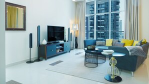 A modern living room with a large window, a flat-screen TV, a sofa with cushions, a coffee table, and a floor lamp. - Maison Privee - Beautiful Chic Apt w/Full Marina View Nxt 2 Beach (Dubai)