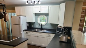 A compact kitchen with white cabinets, a black countertop, a built-in microwave, and a coffee maker. - Greenlodge Cottage - Grand Bend, Ontario, Canada (Zurich)
