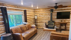 A log cabin interior with a leather sofa, a television, a fireplace, and a ceiling fan. - Greenlodge Cottage - Grand Bend, Ontario, Canada (Zurich)