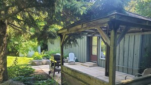 A wooden pergola with a bench, a covered patio area, and a view of a backyard with a lawn and trees. - Greenlodge Cottage - Grand Bend, Ontario, Canada (Zurich)