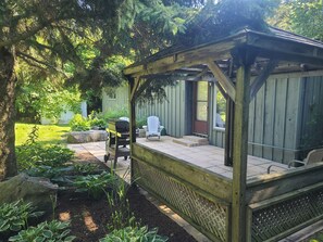 A wooden pergola with a bench, a covered patio area, and a view of a backyard with a lawn and trees. - Greenlodge Cottage - Grand Bend, Ontario, Canada (Zurich)