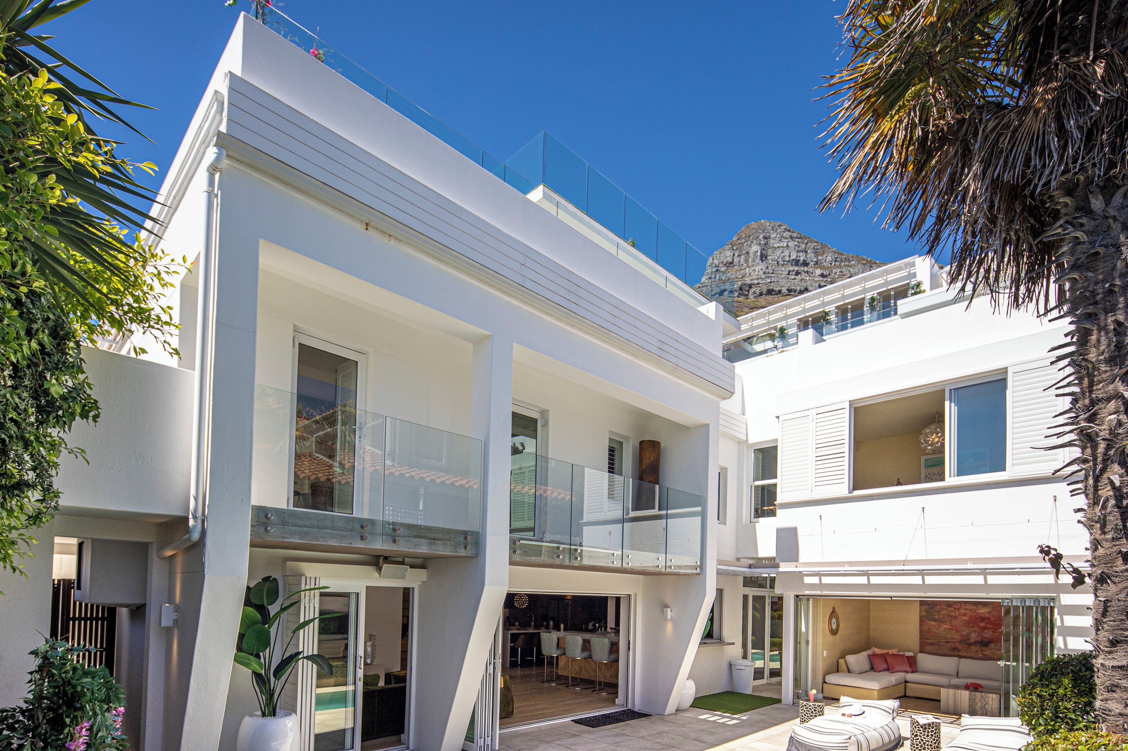 A modern two-story building with a balcony, a pool, and a dining area.