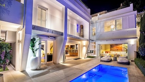 Ein modernes, zweistöckiges Haus mit Swimmingpool, großen Fenstern und einem hellen Innenraum.