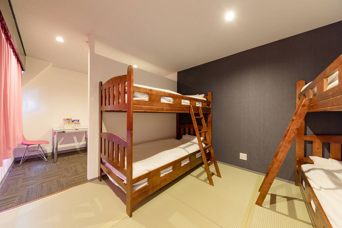 A bunk bed room with a desk and chair, a ladder, and a tatami mat floor.