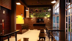 A restaurant interior with wooden benches, a stone wall, and a view through large windows. - Casa Lake View Resort (Vythiri)