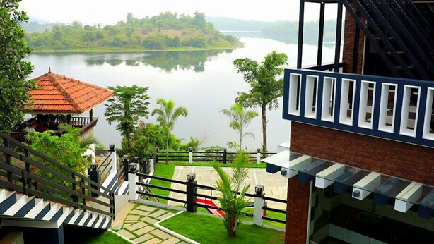 A view from a balcony overlooking a lake with a traditional building and a modern structure with large windows. - Casa Lake View Resort (Vythiri)