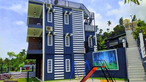 A multi-story building with a blue and white facade, a playground with slides and swings, and a staircase leading to an upper level. - Casa Lake View Resort (Vythiri)