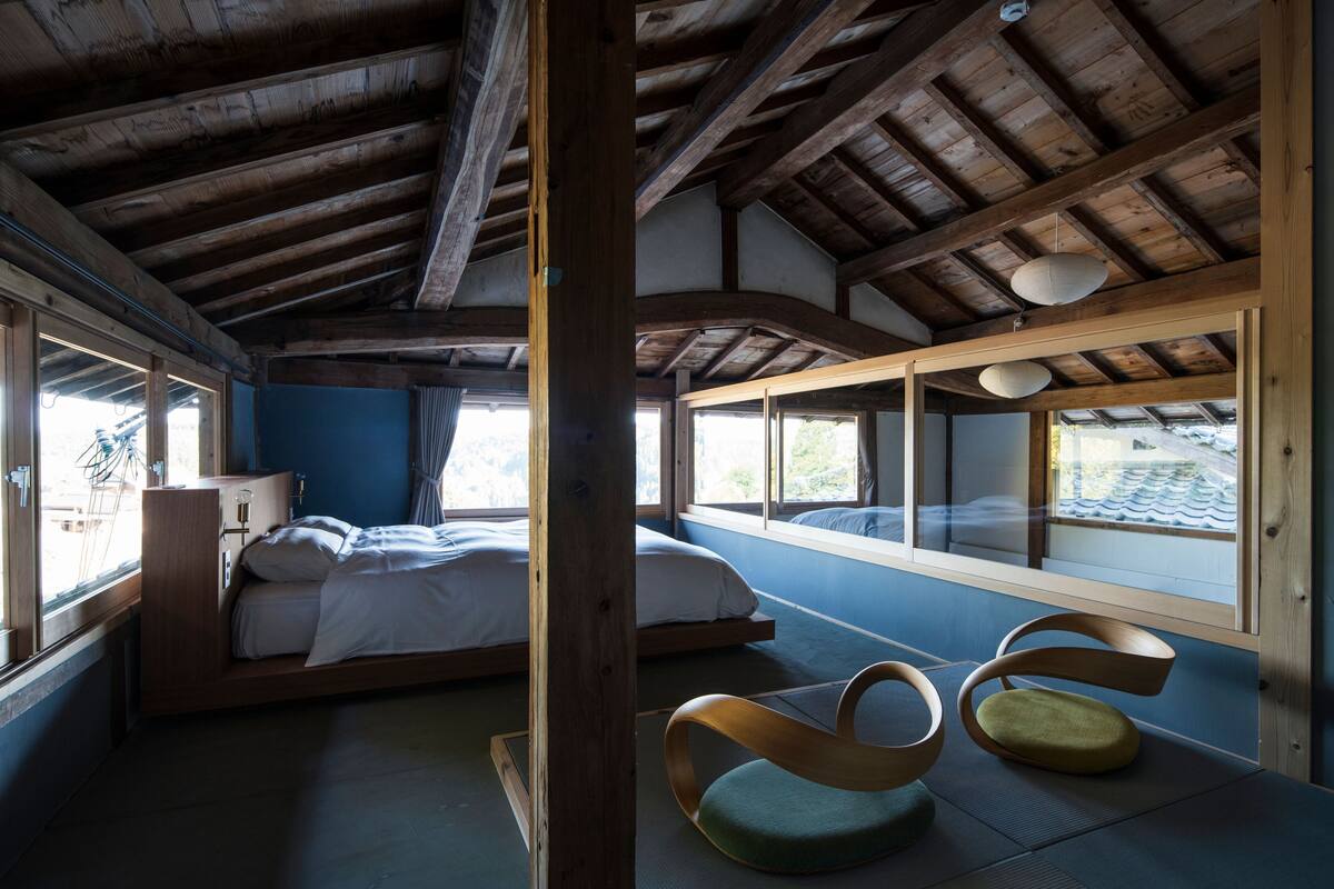 A room with a wooden ceiling, a bed, a window, and a chair.