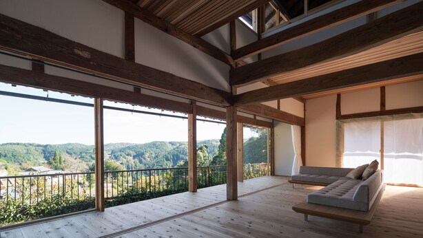 Amplia habitación con piso de madera y grandes ventanas que ofrecen vistas a un valle boscoso.