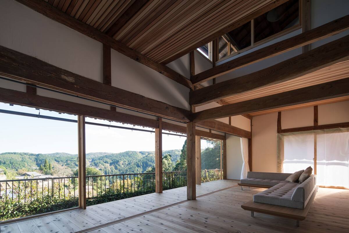 A spacious room with a wooden floor and large windows offering a view of a forested valley.