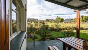 A wooden bench and table outside a building with a view of a grassy field and hills in the distance. - Karoohuisie (Kopanong)
