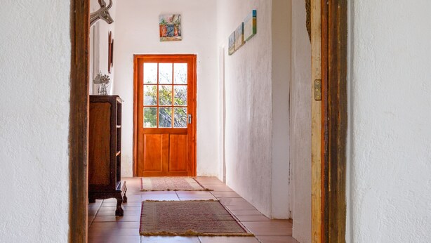 An arched doorway leading to a room with a wooden door, a tiled floor, and a small rug. - Karoohuisie (Kopanong)