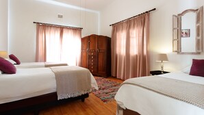 A hotel room with two beds, a wooden wardrobe, a patterned rug, and a nightstand with a lamp. - Karoohuisie (Kopanong)