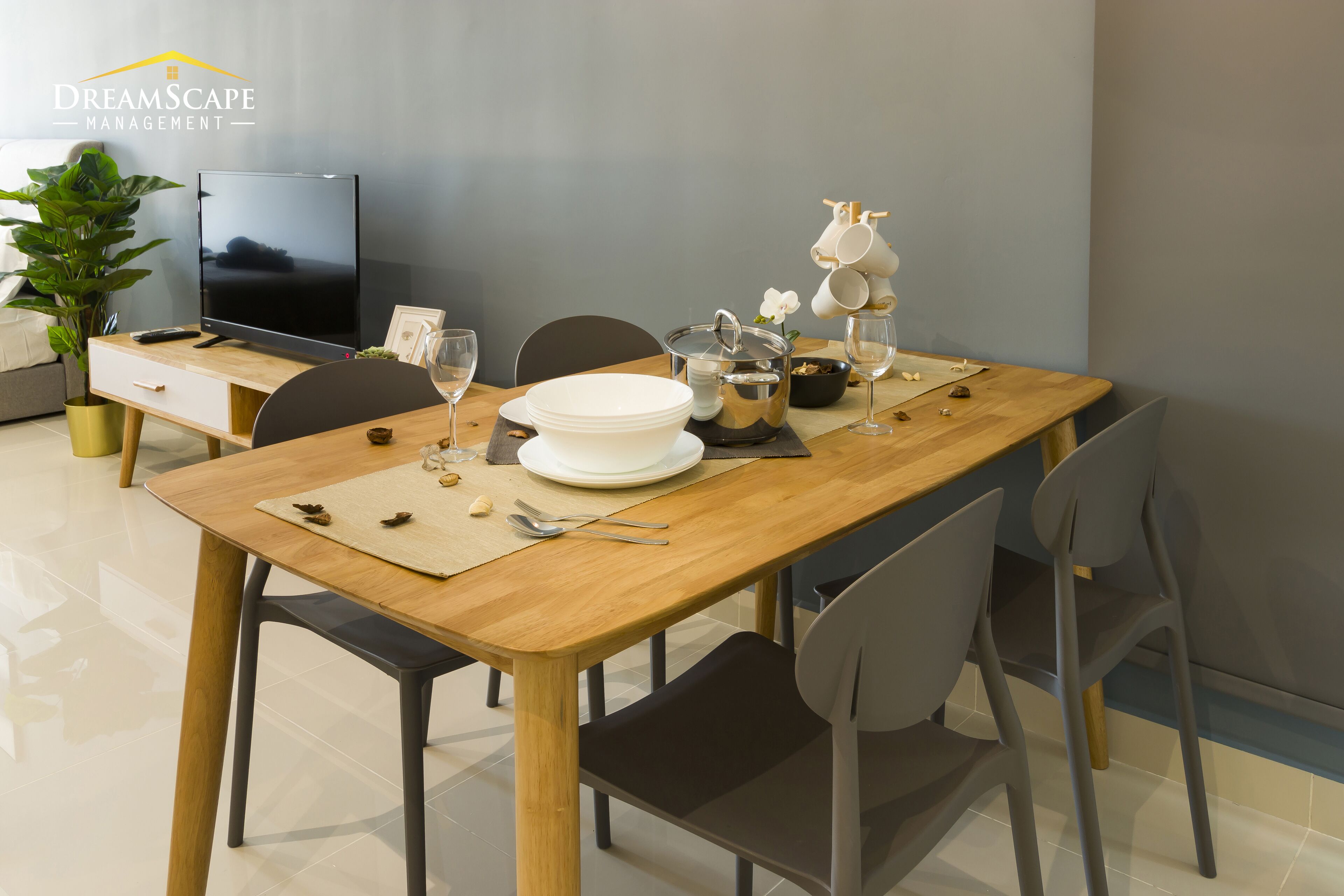 A dining area with a wooden table, chairs, a television, and a potted plant.