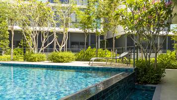 A swimming pool with a tiled edge, surrounded by greenery and a building with balconies.