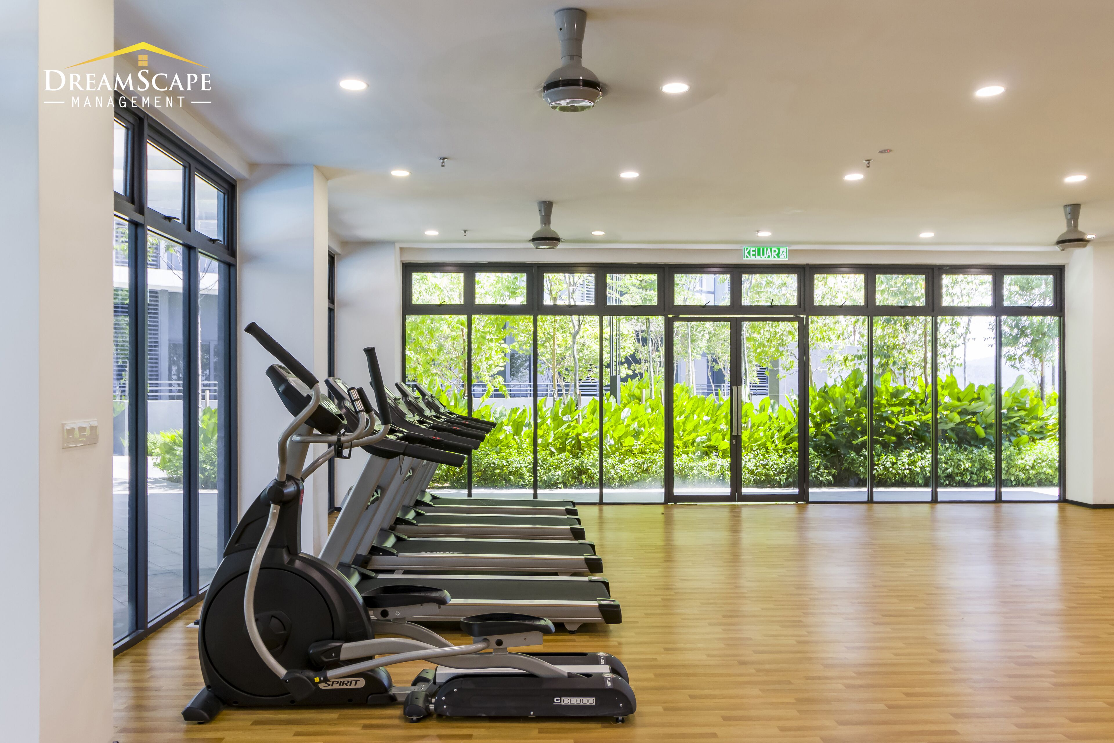 A gym with multiple treadmills aligned against a wall with large windows, a wooden floor, and a ceiling with recessed lighting.