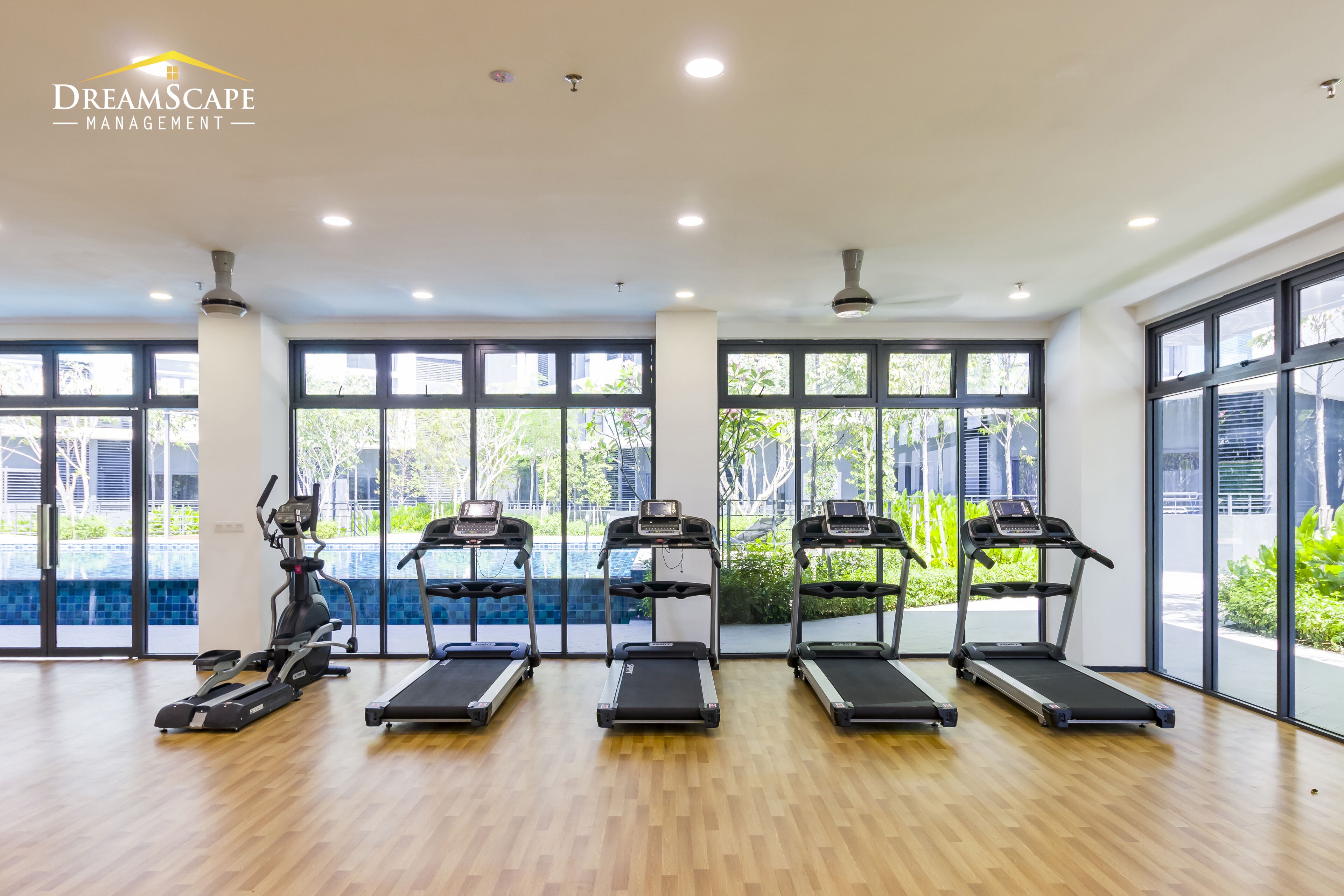 Un gimnasio con cintas de correr, máquinas elípticas y un remo. Cuenta con ventanas amplias y piso de madera.