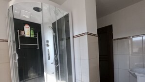Un baño moderno con ducha de vidrio, paredes de azulejos blancos y un lavamanos blanco.