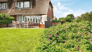 Una casa tradizionale con tetto di paglia, un patio con mobili da esterno e un giardino pieno di fiori.