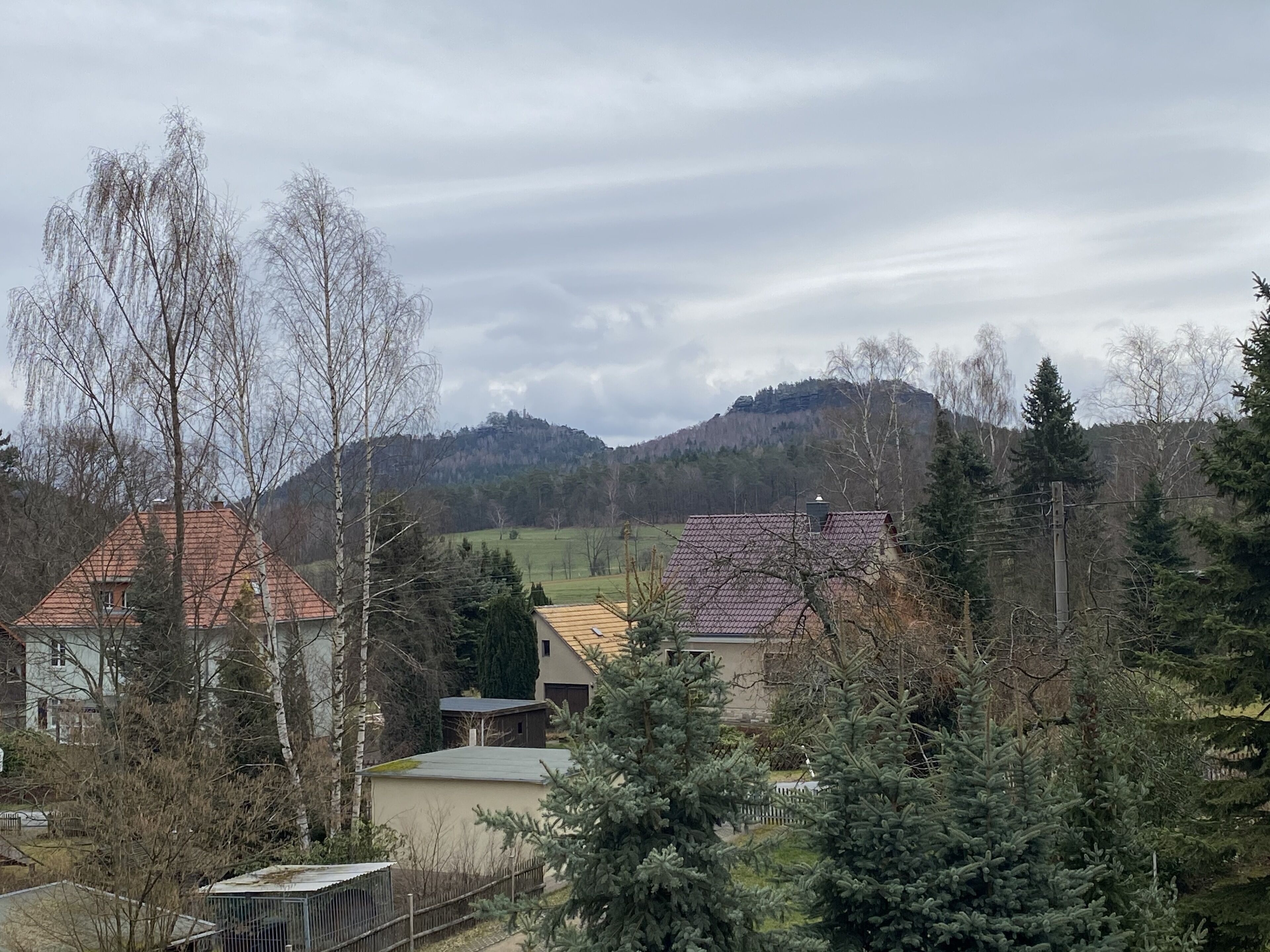 A rural landscape with houses, trees, and a hill in the background.