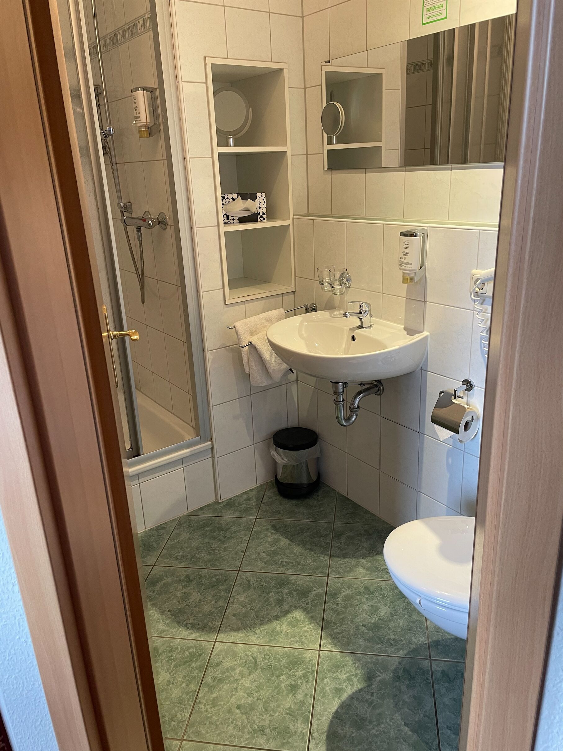 A bathroom with a shower, sink, toilet, and a trash bin.