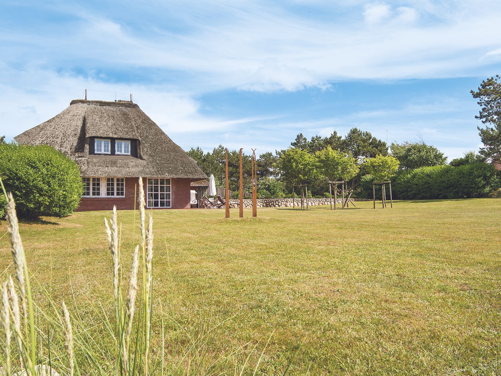 A thatched-roof house with a brick lower level, surrounded by a grassy field and trees.