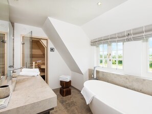 Ein modernes Badezimmer mit freistehender Badewanne, einer Duschkabine aus Glas und einer Holztreppe, die zu einem Erker führt.