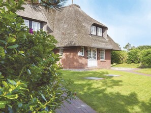 Ein reetgedecktes Haus mit Backsteinfassade, einer Haustür und einer kleinen Veranda.