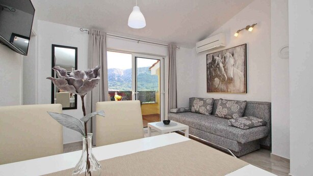 A modern living room with a sofa, a dining table with a vase, a flat-screen TV, and a painting on the wall. - Holiday apartment modernly furnished only 300 m from the sea (Baška)