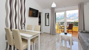 A modern living room with a dining area, a sofa, and a balcony with a view of mountains. - Holiday apartment modernly furnished only 300 m from the sea (Baška)
