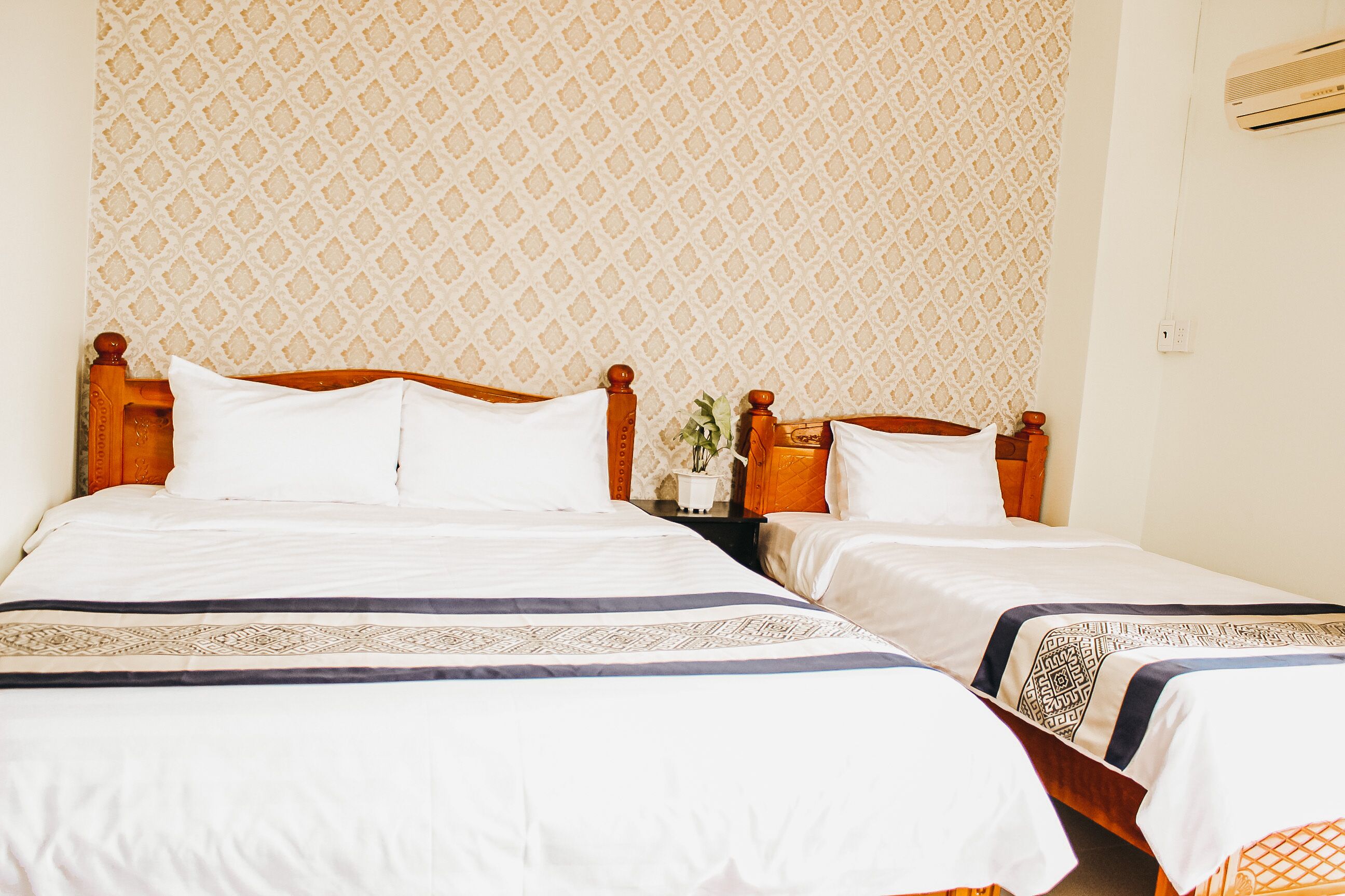 A double bed with a wooden headboard, a nightstand with a lamp, and a patterned wall.