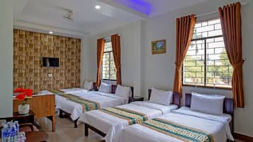 Habitación de hotel con tres camas, un televisor, un escritorio con un florero y una ventana con cortinas.