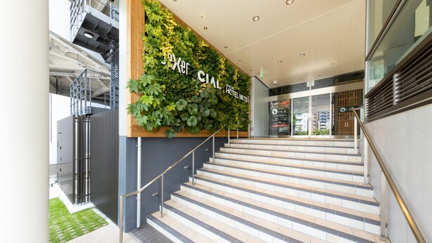 A modern hotel entrance with a staircase leading to the lobby, a vertical garden, and a sign reading "Hotel Metis."
