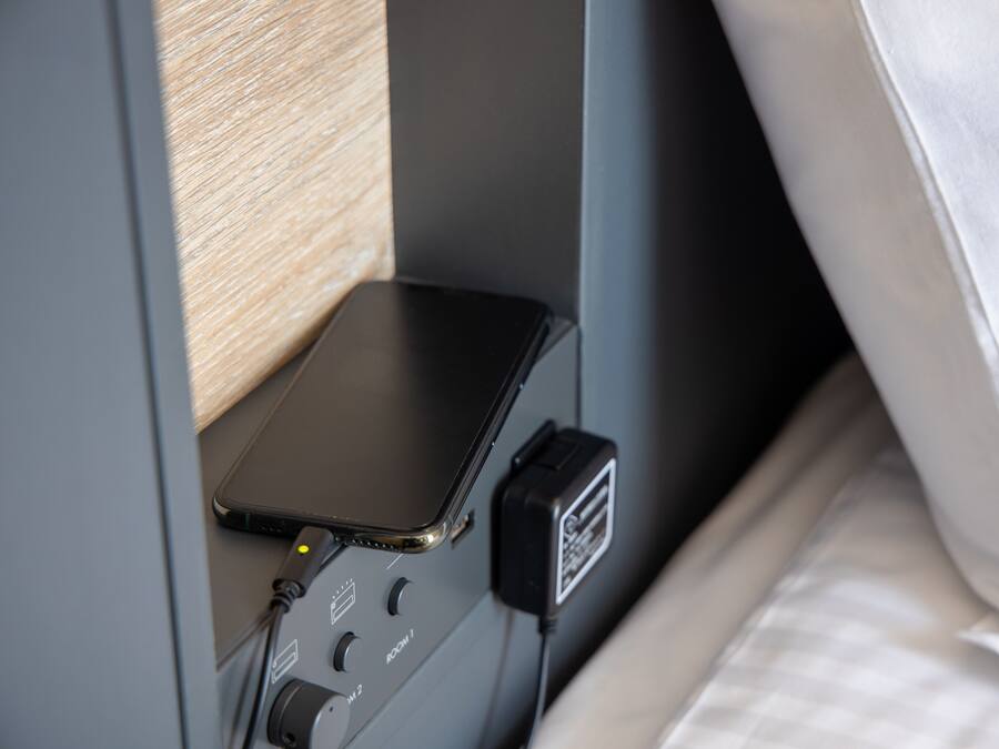 A bed with a white sheet and a small table with a black device on it.