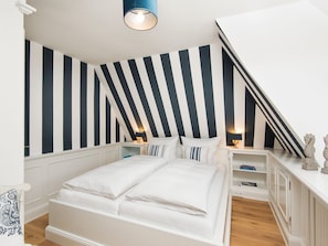 Ein Schlafzimmer mit einem Bett, zwei Nachttischen mit Lampen, einer weißen Kommode und einer gestreiften Wand.
