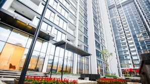 Un edificio moderno con varios pisos, amplias ventanas y terrazas exteriores con flores rojas.