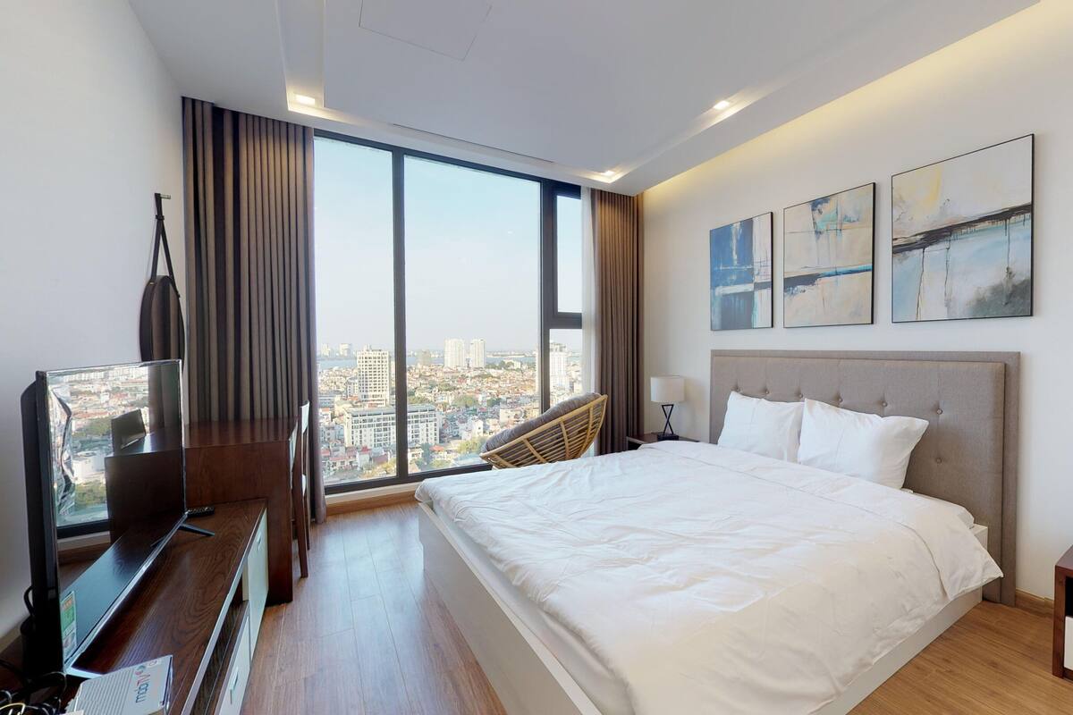 A modern hotel room with a large bed, a TV, and a view of the cityscape.